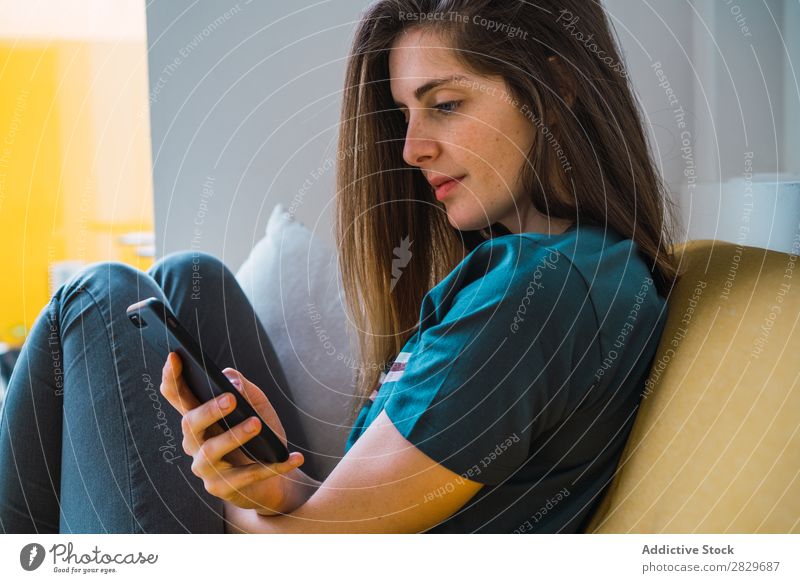Cheerful girl with phone relaxing on sofa Woman Couch Lounge PDA Contentment Happiness using texting messaging Posture Relaxation Internet Comfortable