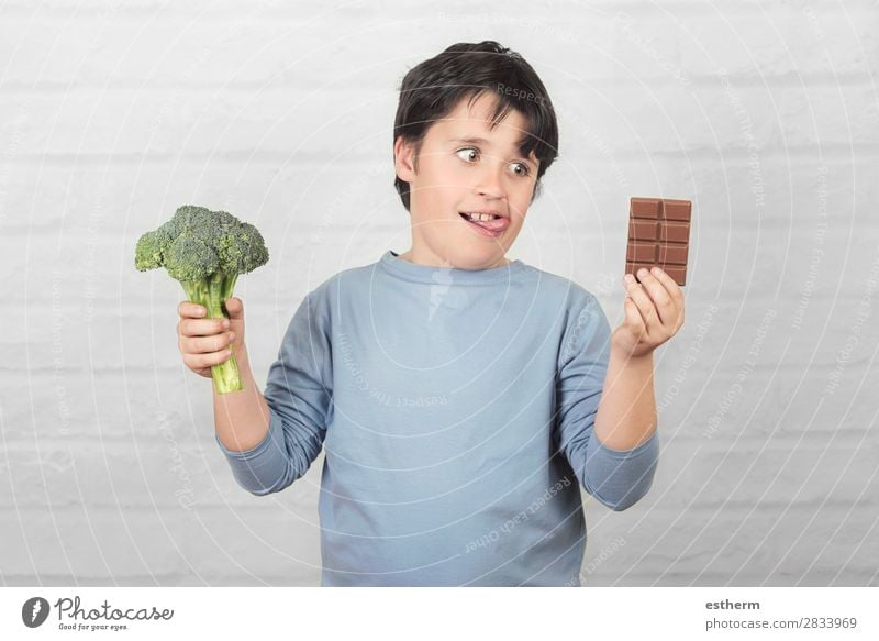 Hungry child with broccoli and an chocolate bar in his hands against brick background Food Vegetable Dessert Chocolate Nutrition Eating Vegetarian diet Diet