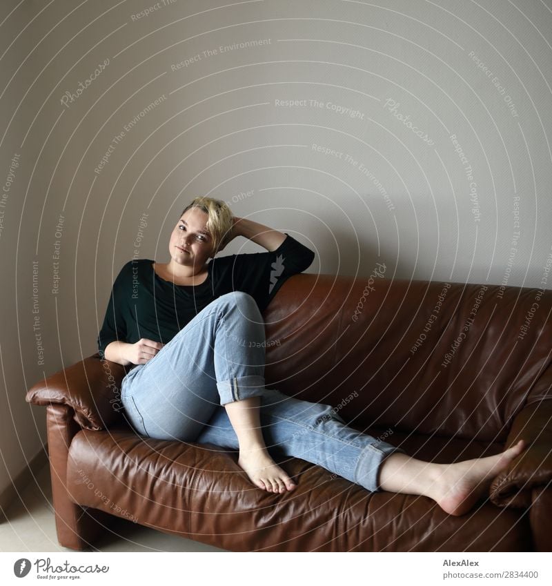 Young woman sits on the couch and stretches out her long legs Style Joy pretty Contentment Sofa Room Youth (Young adults) 18 - 30 years Adults Jeans Barefoot