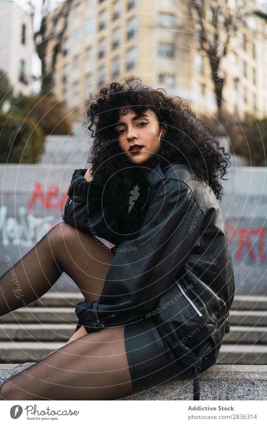 Cheerful woman sitting on wall Woman Attractive City fashionable Curly Brunette Wall (building) Fence Sit Jacket Fashion Youth (Young adults) Beautiful pretty