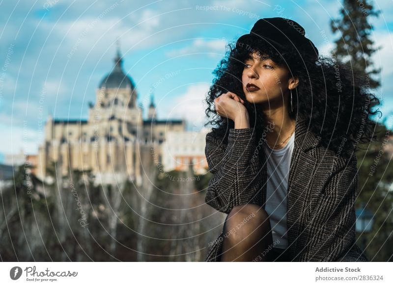 Young stylish woman sitting in city Woman Attractive City fashionable Curly Brunette Coat Hat Sit Fence Vantage point Fashion Youth (Young adults) Beautiful