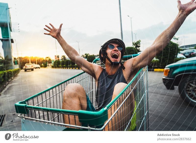 Emotional man in shopping cart Man Shopping Trolley riding Cart pushcart Sunglasses shopper Ride handsome Cheerful Joy Parking lot Human being Markets Humor