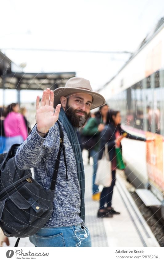 Cheerful tourist on train station Man Tourist Railroad Station Welcome Gesture Goodbye Looking into the camera Vacation & Travel Transport Trip Backpack