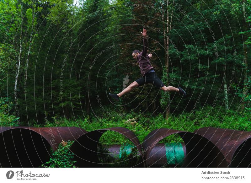 Man jumping on huge tube Tube Stand Piece Metal Pipe Industrial Jump Running Action in motion tracer Fitness Athletic Self-confident Human being Forest Nature