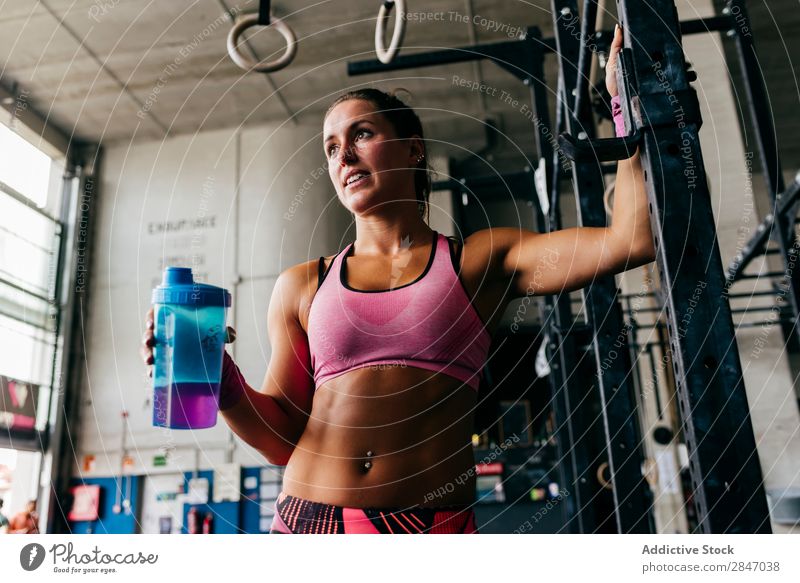 Smiling girl drinking in gym Woman Drinking Gymnasium Refreshment Fitness Healthy Athletic Body workout Bottle Contentment Cheerful Posture Strong Muscular