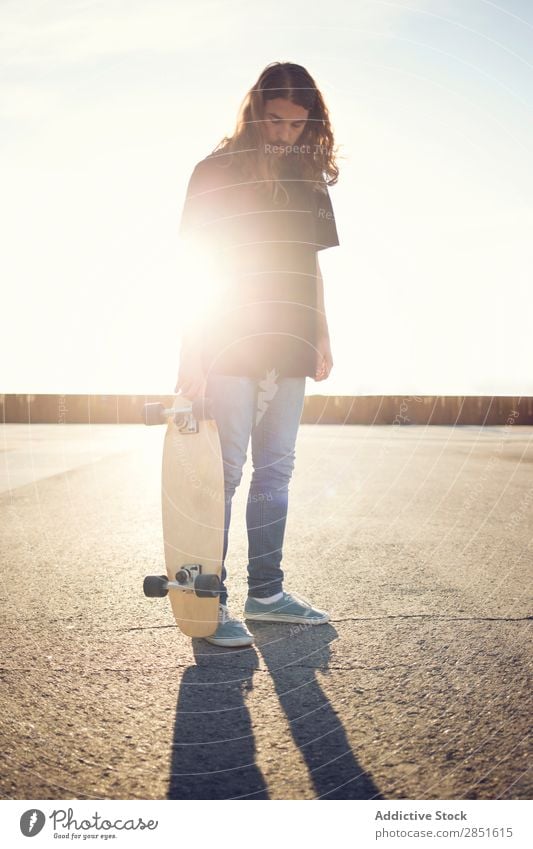 Man posing with skateboard in evening Skateboarding Ice-skating long hair Square Asphalt Evening Sunset skateboarder Youth (Young adults) Lifestyle Joy Extreme