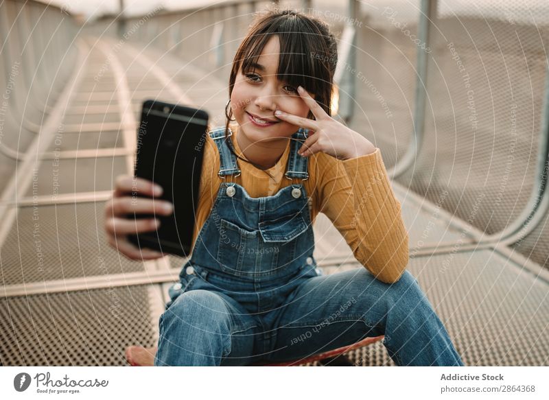 Funny girl taking selfie on smartphone on walkway Youth (Young adults) PDA Corridor making face Girl jean overall Footpath City Style Cellphone Sit Town