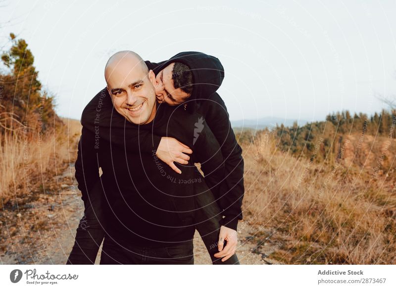 Smiling man holding on back cheerful guy on road on hill Homosexual Couple Embrace Back Street Hill having fun Love embracing Mountain Sky Lanes & trails