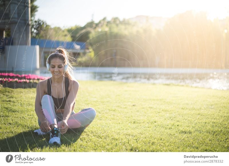 sports woman doing lawn exercises and stretching on the grass outdoor in a park listening music yoga pilate fitness sunset girl young American ethnicity