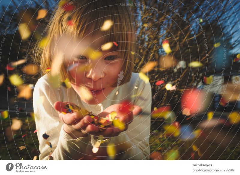 Little girl blows confetti into the camera Carnival Infancy 1 Human being 3 - 8 years Child bushes Garden Blonde Confetti Feasts & Celebrations smile Playing