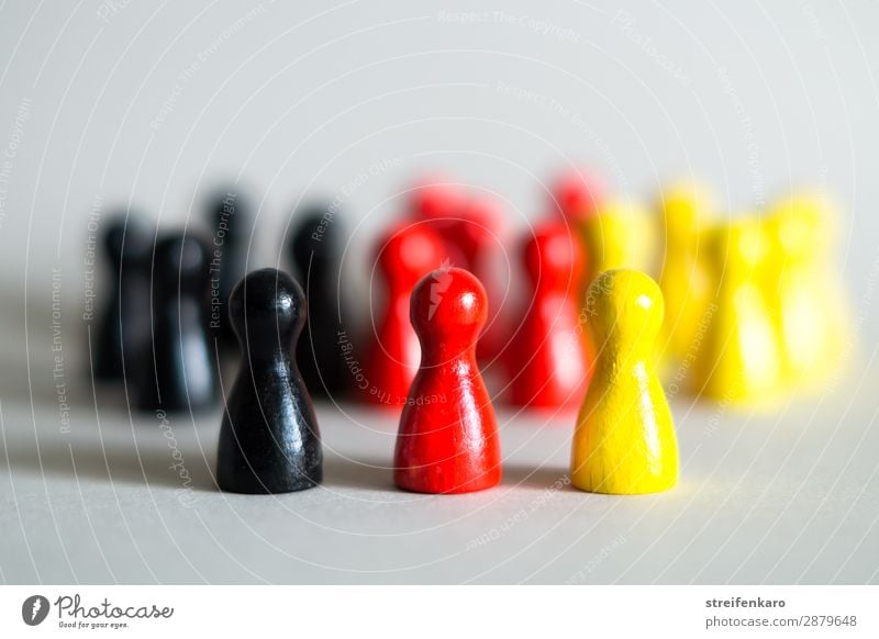 Three game pieces in German colours stand in front of a large group of game pieces in black, red, gold Group Toys Wood Sign Free Yellow Gold Red Black Force