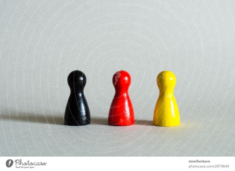 Three game pieces in black, red, yellow stand in a row Toys Wood Sign Flag Stand Yellow Gold Red Black Agreed Society Politics and state Government Germany