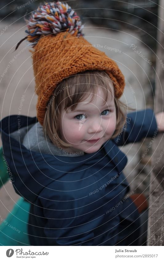 Girl with knitted cap plays in the sand Feminine Toddler 1 Human being 1 - 3 years Earth Spring Winter Bad weather Garden Rain jacket Cap Brunette Short-haired