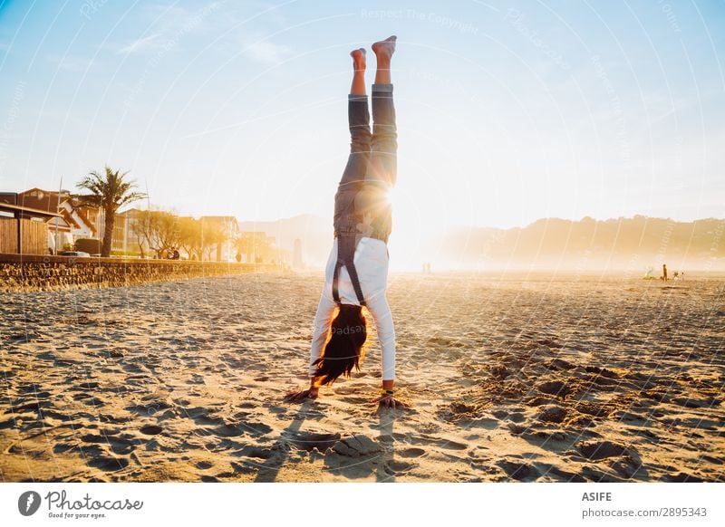 Little girl standing on hands on the beach at sunset Joy Happy Beautiful Playing Vacation & Travel Freedom Summer Beach Ocean Child Nature Sand Sky Coast Jeans