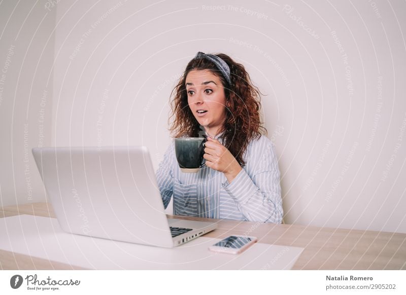 A woman looks surprised at her laptop while holding a cup Coffee Lifestyle Happy Desk Table Work and employment Office Business Telephone Computer Notebook