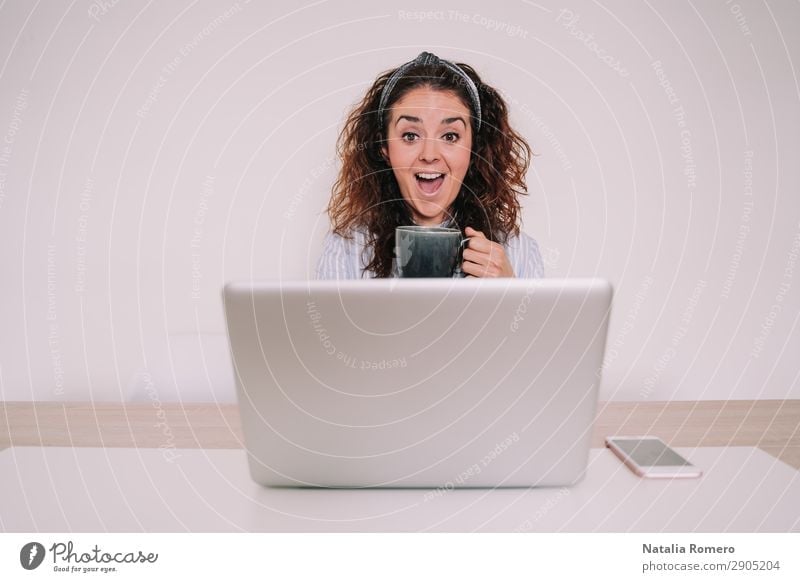 Young woman with a cup in her hand looks surprised at her laptop Coffee Lifestyle Happy Desk Table Work and employment Office Business Telephone Computer