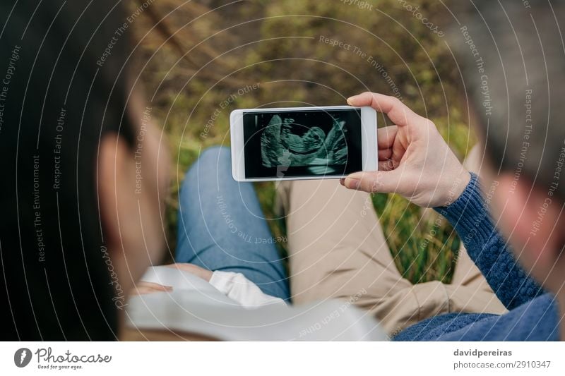 Pregnant looking ultrasound on the mobile with her husband Lifestyle PDA Technology Human being Baby Woman Adults Man Parents Mother Couple Hand Aircraft