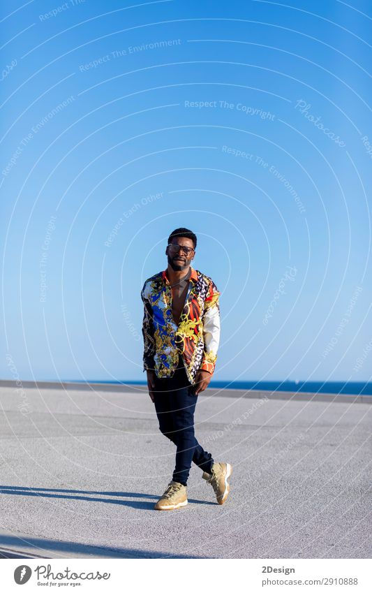 Young black man wearing eyeglasses standing against blue sky Elegant Style Human being Man Adults Clothing Shirt Jeans Eyeglasses Afro Stand Cool (slang)