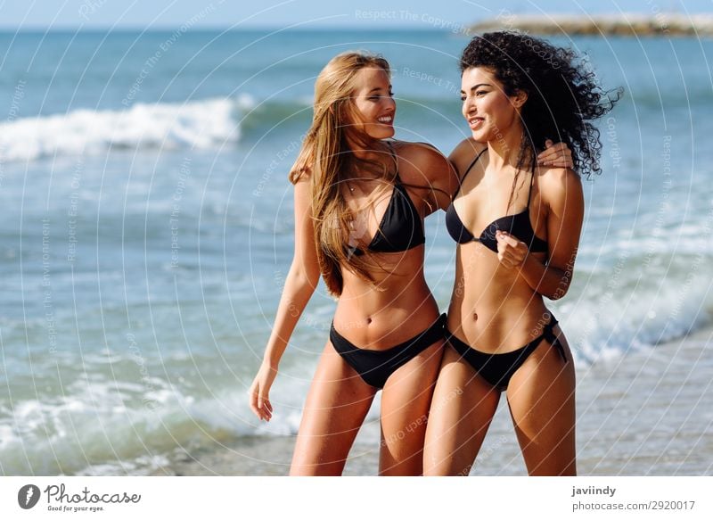 Two young women with beautiful bodies in swimwear on a tropical beach taking a walk on shore. Lifestyle Joy Happy Beautiful Body Hair and hairstyles