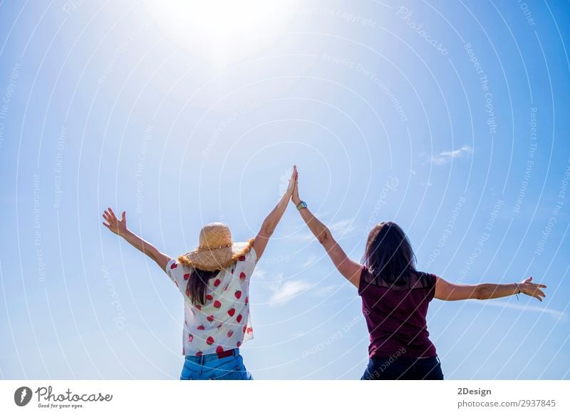 Two young woman sitting on a fence arms raised against blue sky Lifestyle Joy Happy Beautiful Relaxation Leisure and hobbies Vacation & Travel Freedom Summer