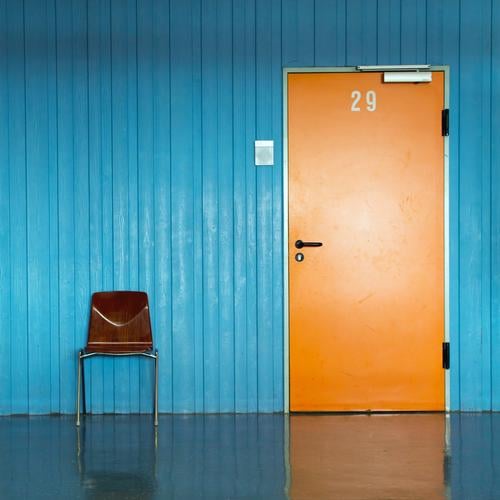 Orange door with number 29 and door sign in blue wall and a chair for waiting people in front of it. Office Chair Classroom Hallway Entrance Digits and numbers