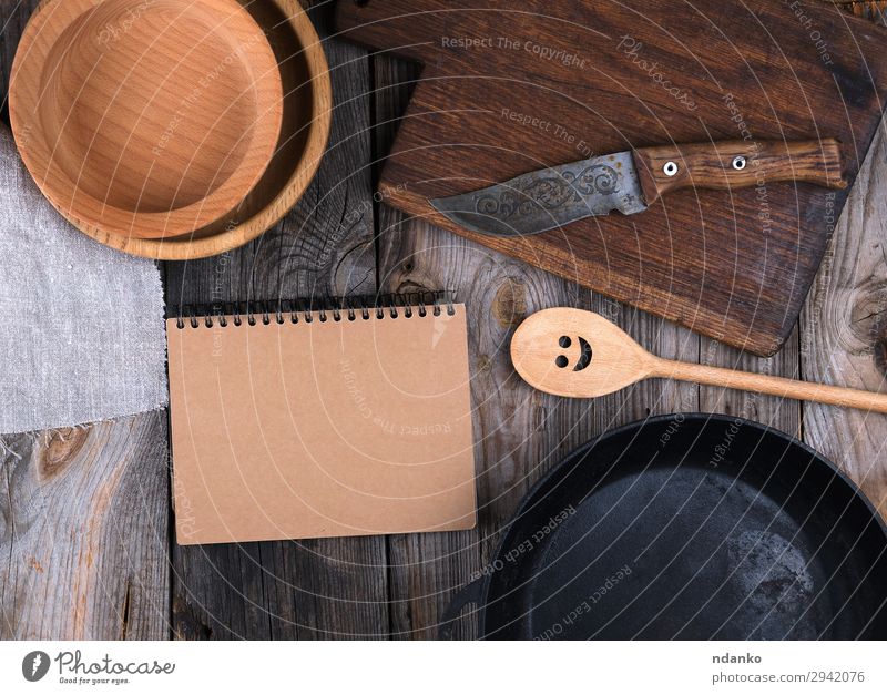 empty black round frying pan, cutting board Plate Pan Knives Spoon Table Kitchen Paper Wood Metal Old Above Clean Brown Gray Black background Cast cooking