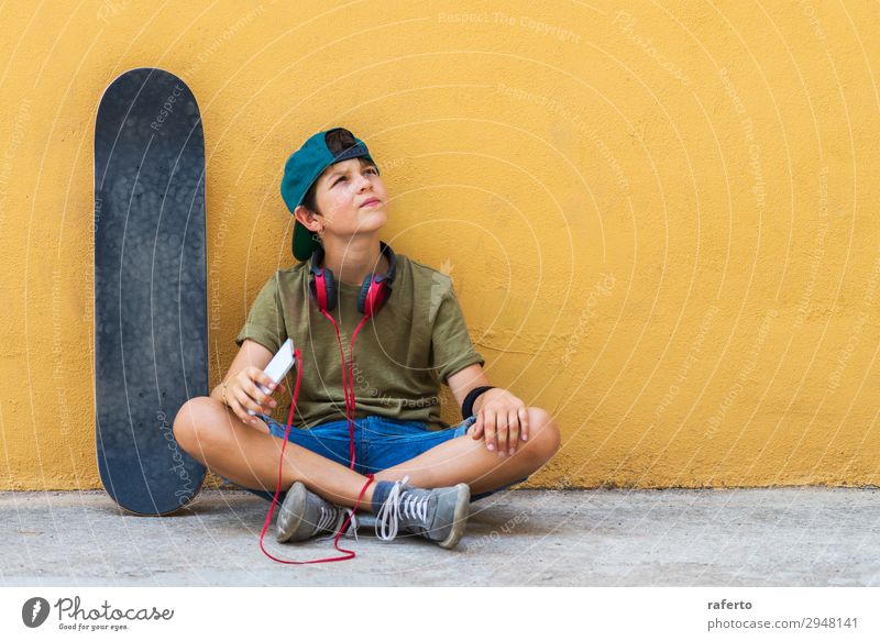 Front view of young boy sitting on ground leaning on a yellow wall while using a mobile phone to listening music Child Telephone PDA Technology Human being