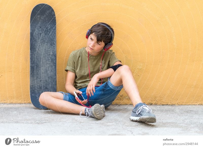 Front view of young skater boy sitting against a yellow wall while listening music by headphones Lifestyle Style Happy Beautiful Leisure and hobbies Freedom