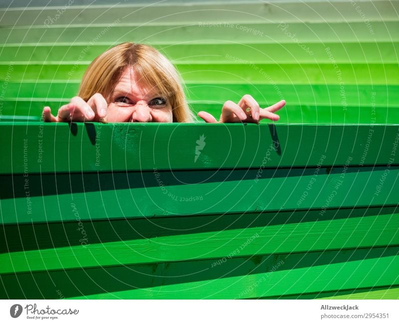Young woman looks carefully over a wooden fence Head Fence Wooden fence Border Spy Looking Observe Caution Green look out look over Hide Hiding place Safety