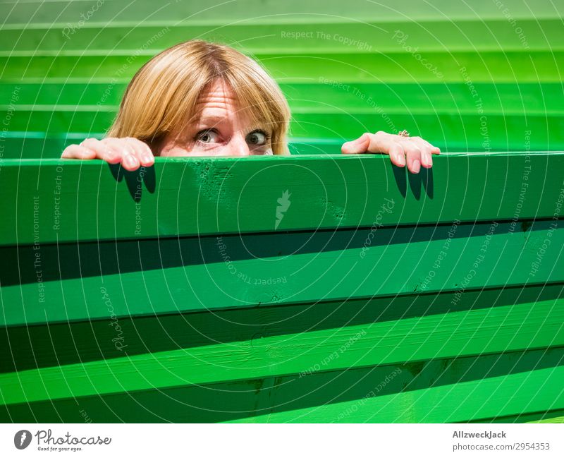 Young woman looks carefully over a wooden fence Head Fence Wooden fence Border Spy Looking Observe Caution Green Timidity Hesitate look out look over Hide