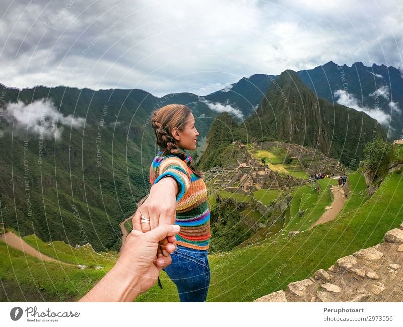 Standing couple holding hands contemplating the terraces over Machu Picchu, the most visited tourist destination in Peru. Rear view image. Vacation & Travel