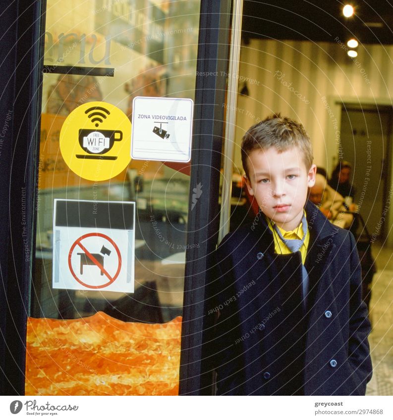 Serious schoolboy at the cafe entrance. Door with sticker signs of free wi-fi, video camera surveillance and animals forbidden. Spain Child Schoolchild Student