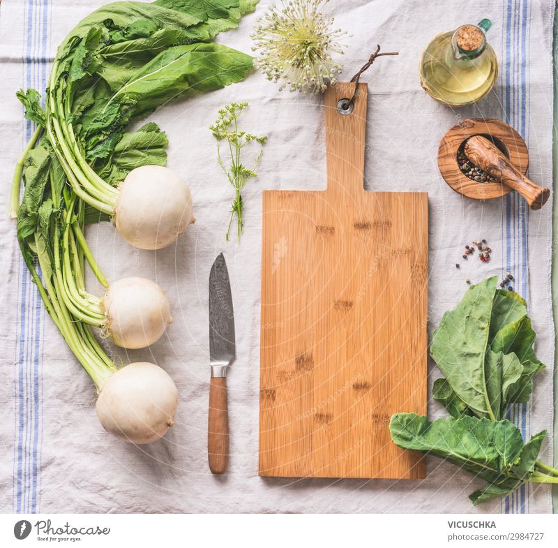 Food background with raw white radish with greens on light kitchen table with cutting board and knife, top view food