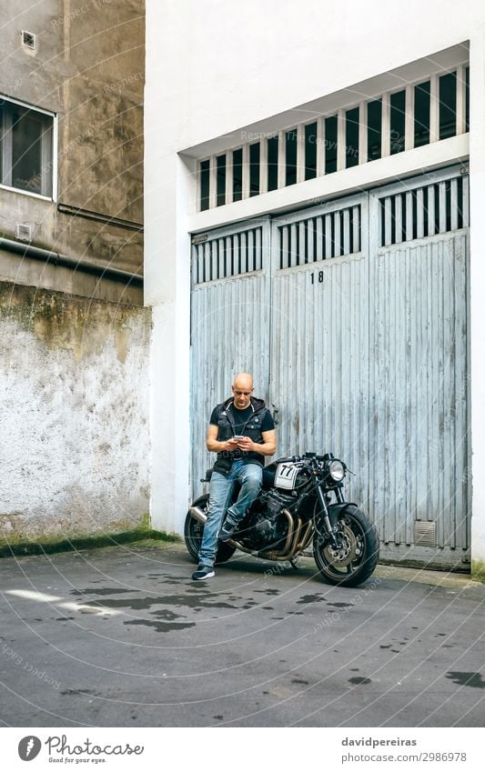 Biker looking mobile sitting on motorcycle Lifestyle Style Trip PDA Engines Human being Man Adults Street Vehicle Motorcycle Sit Wait Authentic Retro Black