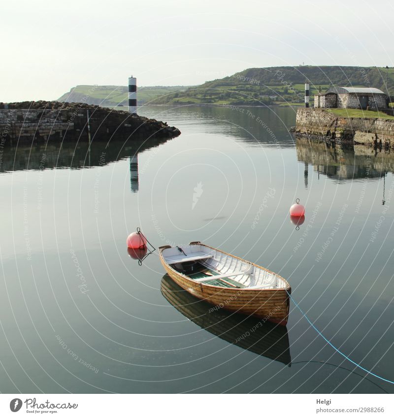 in a small harbour in Ireland a wooden boat lies in still water with reflection, in the background a black and white lighthouse Environment Nature Landscape