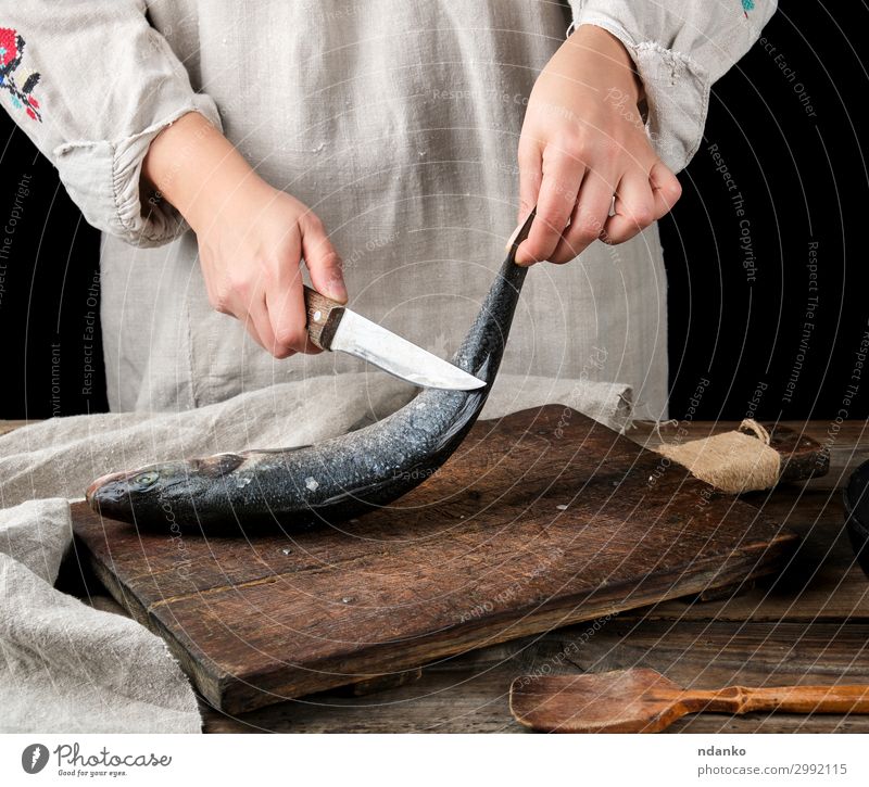 woman in gray linen clothes cleans the fish sea bass Fish Seafood Knives Table Kitchen Tool Woman Adults Hand Fingers Wood Old Make Fresh Clean Brown Gray Black