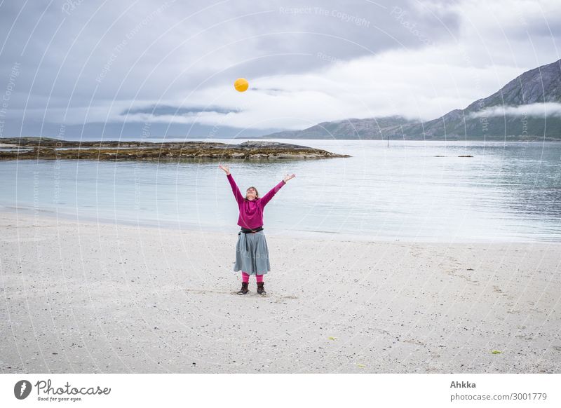 Young woman with outstretched arms throws a yellow ball in the air on the beach by a fjord Concentrate Beach carefree Light heartedness Throw Fjord Freedom