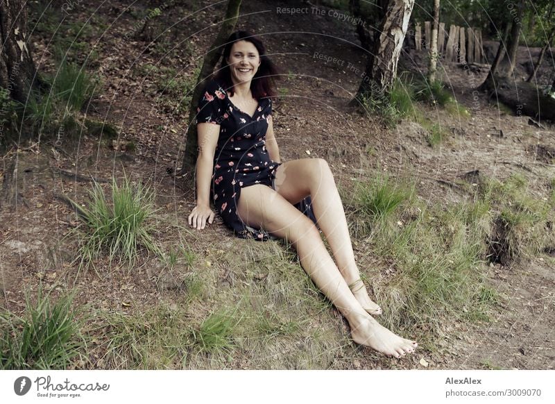 Portrait of a tall young woman sitting smiling in a clearing Lifestyle Joy luck already Young woman Youth (Young adults) Legs 18 - 30 years Adults Nature Plant
