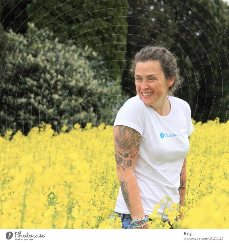 laughing brunette woman with white shirt and tatoos on her arms stands in blooming yellow rape Human being Feminine Woman Adults 1 30 - 45 years Environment