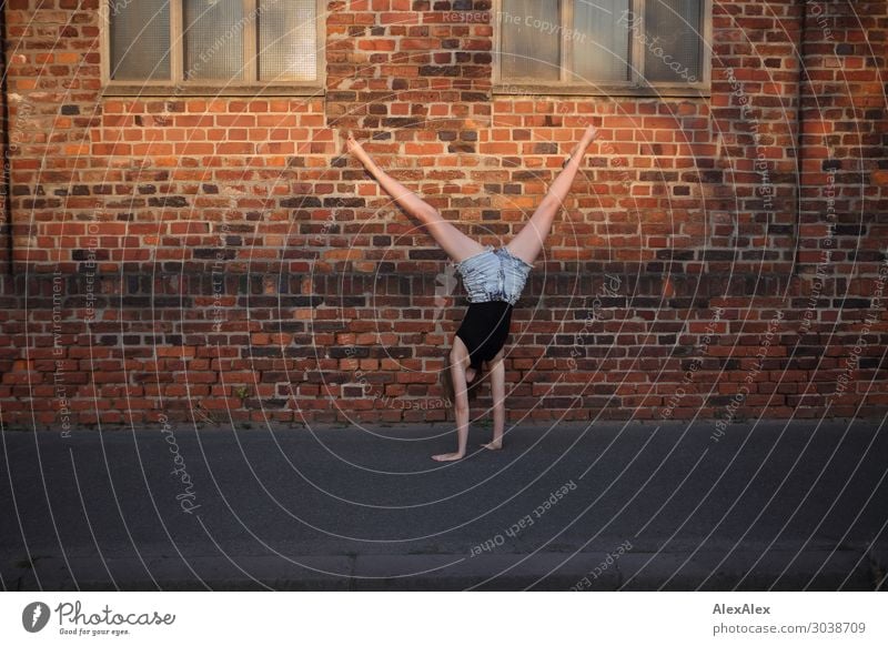 Woman makes a cartwheel in front of a brick wall on the sidewalk Lifestyle Elegant Style Joy pretty Well-being Playing Cartwheel Young woman
