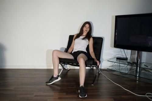 Young woman in an armchair next to a television set Lifestyle Style Living or residing Armchair Room TV set Classical modern Youth (Young adults) Legs
