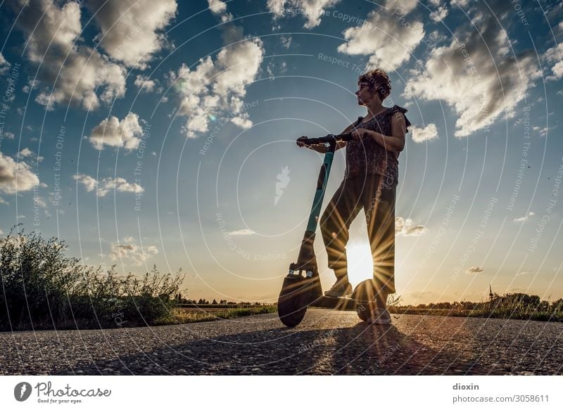 Middle-aged woman stands with e-scooter in front of setting sun and defies | climate change Woman electric scooter Means of transport Transport Mobility