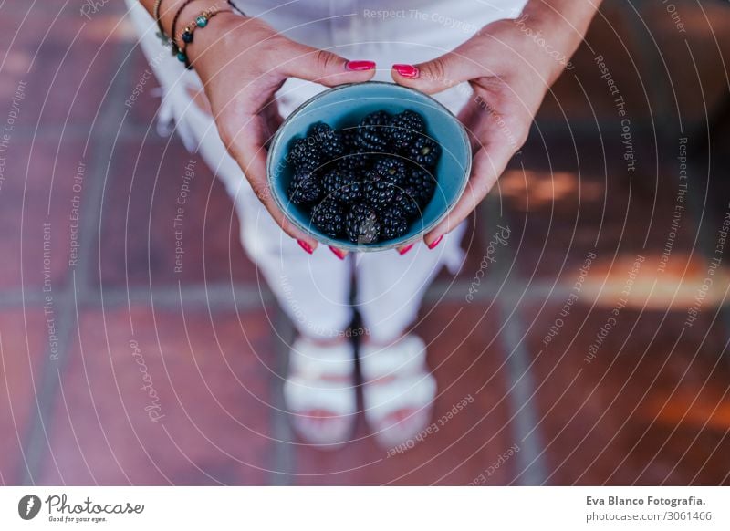 young woman holding a bowl of blackberries. preparing a healthy recipe of diverse fruits, watermelon, orange and blackberries. Using a mixer. Homemade, indoors, healthy lifestyle