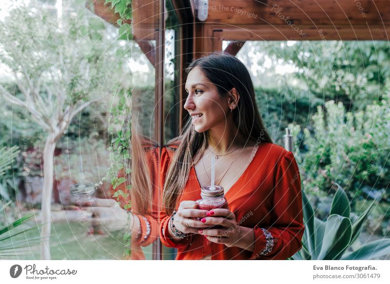 young beautiful woman standing by the window holding a healthy jug of smoothie. Home, indoors and lifestyle Vegetarian diet Drinking Natural Make-up Tasty