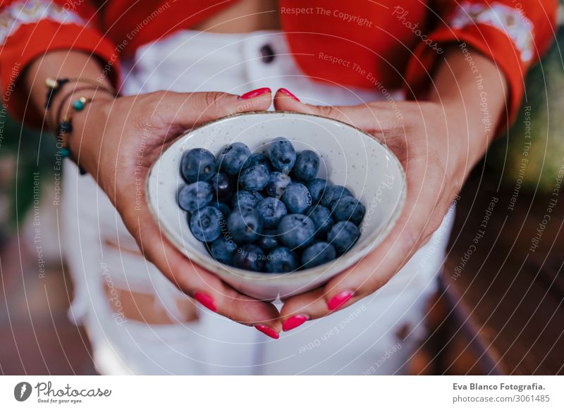 young woman holding a bowl of blueberries. preparing a healthy recipe of diverse fruits, watermelon, orange and blackberries. Using a mixer. Homemade, indoors, healthy lifestyle