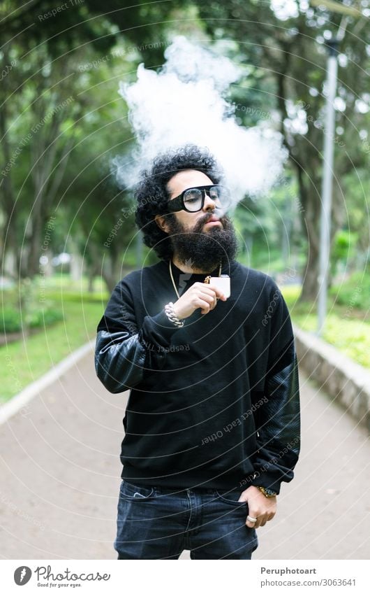 Young man smoking an electronic cigarette in the park. Lifestyle Summer Youth (Young adults) Adults Park Sunglasses Beard Red vape casual smoke steam vaping