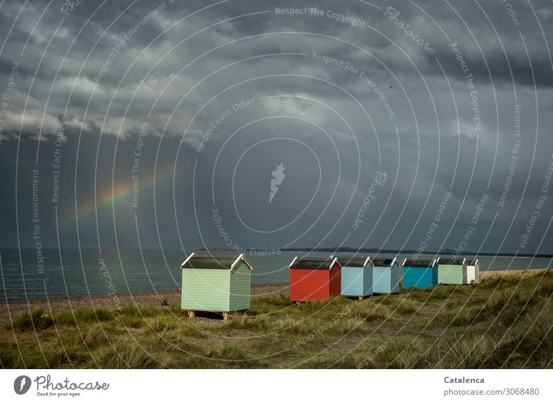 A row of colourful beach huts in the dunes glow as the thunderclouds break up and a rainbow appears Beach Ocean Marram grass Storm clouds Rainbow Horizon
