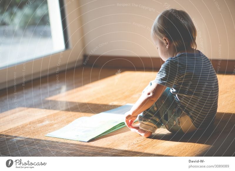 a child sits on the wooden floor and reads a book while the sun shines on it Child Parquet floor Book Reading by oneself at home self-employment tranquillity