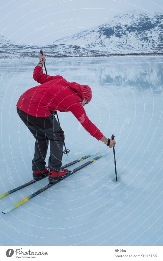Man with red jacket, red shoes and red cap on skis checks ice thickness of a lake with a ski pole Aquatics Winter sports Skis Science & Research