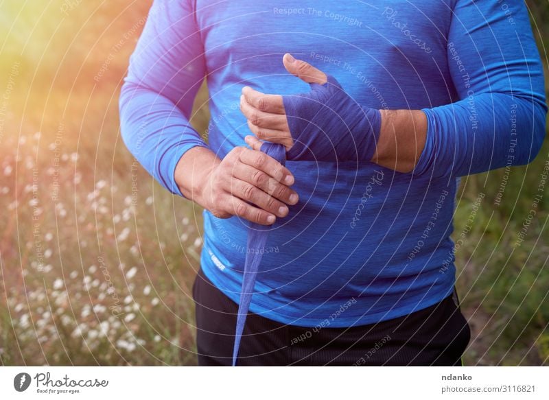 athlete stand and wrap his hands in blue bandage Lifestyle Body Athletic Leisure and hobbies Summer Sports Human being Masculine Man Adults Hand Grass Fitness
